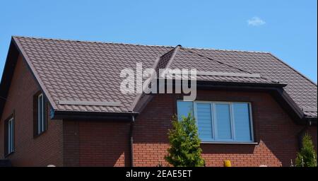 Eine Nahaufnahme auf einem braunen Mansardendach aus Metall mit Schneewächtern, Schneestopfen eines Ziegelhauses gegen den blauen Himmel. Stockfoto