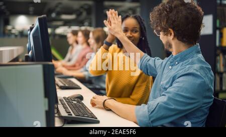 Universitätsbibliothek: Bright Black Girl und Smart Hispanic Boy zusammen arbeiten an Computern, geben High-Five nach erfolgreich abgeschlossen Aufgabe. Schüler Stockfoto