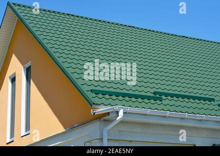 Dachrinne defekt. Eine Nahaufnahme auf Metall gekacheltem Giebeldach mit Schneestoppern, gebrochenem Regenrinnensystem und Dachfenster eines Hauses. Stockfoto