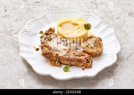 Portion Kartoffelpüree und gebratenes Schweinefleisch auf weißem Teller Stockfoto