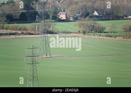 Strommasten mit hängenden Kabeln säumten grüne Felder in Pewsey Vale, Wiltshire Stockfoto