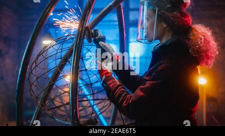 Portrait of Talented Emerging Female Artist nutzt einen Disc Grinder, um eine abstrakte, brutale Metallskulptur zu machen, die den gegenwärtigen Moment widerspiegelt Stockfoto