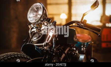 Nahaufnahme Details eines Custom Bobber Motorrads stehen in einem authentischen kreativen Workshop. Verchromte Motorrad-Scheinwerfer, Griffstangen und Stoßdämpfer Stockfoto