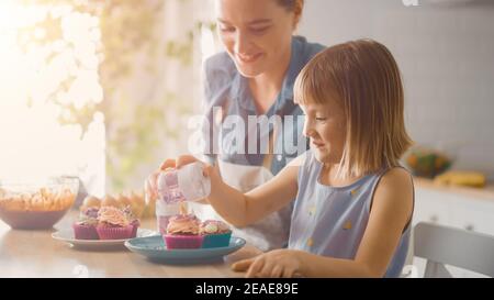 In der Küche: Mutter und nette kleine Tochter bestreuen Funfetti auf cremigen Cupcakes Frosting. Sie Haben Spaß Kochen Muffins Zusammen. Kind Stockfoto