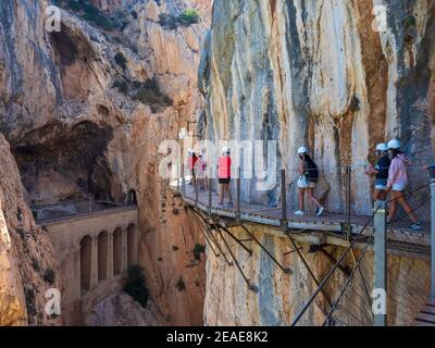 Wandergruppe mit Helm und Masken entlang des Caminito del Rey in der Gaitanes-Schlucht in Malaga. Stockfoto