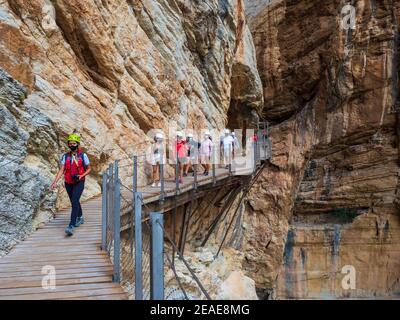 Wandergruppe mit Helm und Masken entlang des Caminito del Rey in der Gaitanes-Schlucht in Malaga. Stockfoto