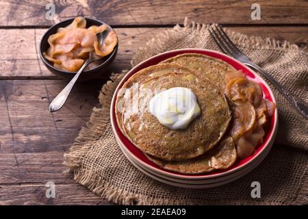 Vegetarische Buchweizenpfannkuchen mit gebackenen Äpfeln mit Zimt, Honig und frischer Sahne auf einem Holztisch, rustikalen Stil, horizontal. Lecker gesund fo Stockfoto