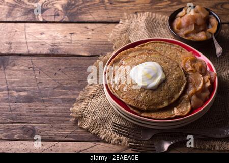 Vegetarische Buchweizenpfannkuchen mit gebackenen Äpfeln mit Zimt, Honig und frischer Sahne auf einem Holztisch, rustikaler Stil, Freiraum. Lecker gesund fo Stockfoto