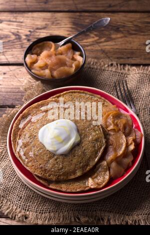 Vegetarische Buchweizenpfannkuchen mit gebackenen Äpfeln mit Zimt, Honig und frischer Sahne auf einem Holztisch, rustikaler Stil, vertikal. Leckeres gesundes Essen Stockfoto