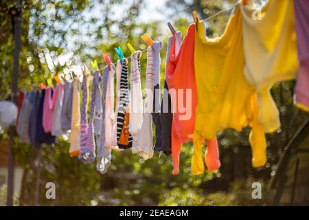 Baby niedliche Kleidung hängen auf der Wäscheleine im Freien. Kinder Wäsche hängt auf Linie im Garten auf grünem Hintergrund.Baby Zubehör. Stockfoto