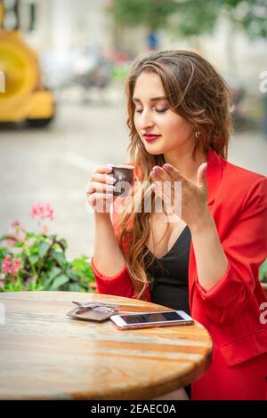 Schöne junge Frau schnüffeln Kaffee in einer kleinen Tasse und Kaffee trinken sitzen am Tisch in einem Café im Freien Stockfoto