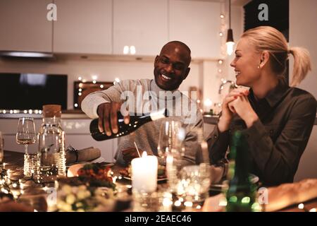 Mann Gießen einen Freund ein Glas Wein während einer Candlelight Dinner Party um einen Tisch mit Freunden Stockfoto