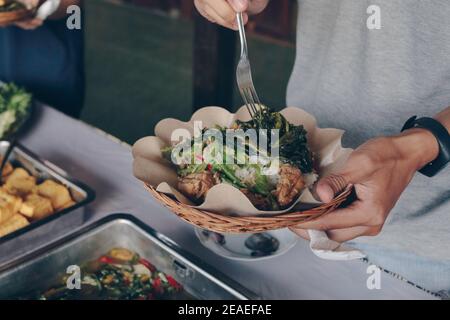 Person Hand legt weißes Gemüse aus der Stahlpfanne zu Hölzerner Pappteller während des Mittagessens im Restaurant Stockfoto