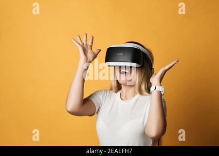 Aufgeregt glücklich schreiende blonde Frau in weißem T-Shirt verwendet VR Brillen, die Augmented Reality erkunden, halten die Hände hoch Stockfoto