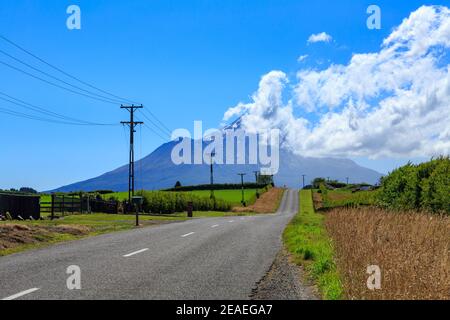 Eine Straße, die zum Mount Taranaki, Neuseeland führt. Sommerwolken wirbeln um den Gipfel des Berges Stockfoto