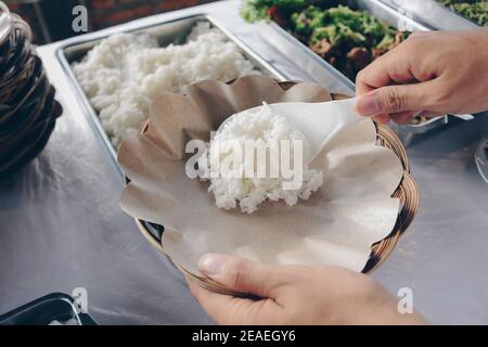 Person Hand legt weißen Reis aus der Stahlpfanne zu Hölzerner Pappteller während des Mittagessens im Restaurant Stockfoto