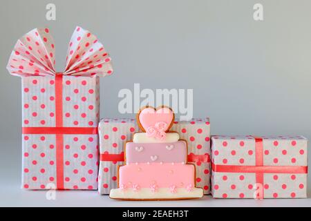 Schöne rosa Schachteln für Geschenke mit einem Band ein Lebkuchen Kuchen auf einem grauen Hintergrund. Red Box, Feiertagskonzept, Valentinstag, Hochzeit, Geburtstag Stockfoto