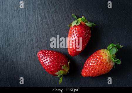 Frische, saftige Erdbeeren, drei Stück, in der Nähe liegend, auf Marmorsteinboden. Stockfoto