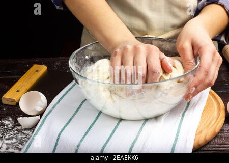 Der Prozess der Herstellung von Hefeteig für Brot. Die Frau knetet den Teig. Die Hände des Bäckers bereiten den Teig vor. Der Prozess der Arbeit in einem Stockfoto