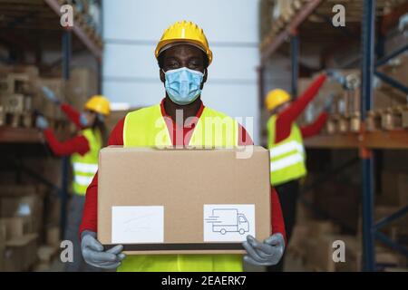 Schwarzer Mann, der im Lager arbeitet und beim Tragen Lieferkisten lastet Gesicht chirurgische Maske während Corona-Virus Pandemie - Logistic und Branchenkonzept Stockfoto