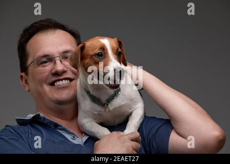 Lässiger junger Mann, der einen Welpen in den Händen hält, während er die Kamera anschaut und lächelt. Auf grauem Hintergrund. Stockfoto