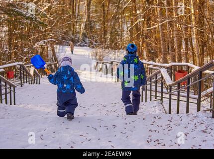 Zwei kleine Kinder in Jumpsuits laufen an einem sonnigen Wintertag die Treppe hinunter. Stockfoto
