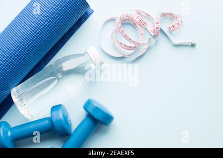 Yogamatte, Dunbells, Messart und Wasserflasche auf blauem Hintergrund. Gewichtsverlust, Fitness, Sport-Konzept. Draufsicht. Speicherplatz kopieren. Stockfoto