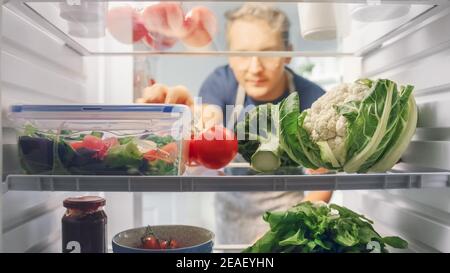 Handsome Young man öffnet Kühlschrank voll von Bio-Lebensmittel und greift ein paar Gemüse für einen Salat. Ernährung und gesunde Lebensweise Konzept. POV aus Stockfoto