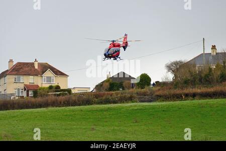 Devon Air Ambulance Hubschrauber Start von einem Feld neben Häusern. Stockfoto