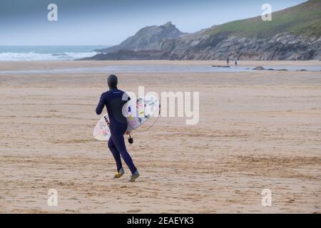 Ein Surfer mit seinem Surfbrett und läuft über Crantock Beach in Newquay in Cornwall. Stockfoto