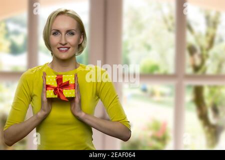 Fröhliche reife Frau hält eine kleine gelbe Geschenkbox. Stockfoto