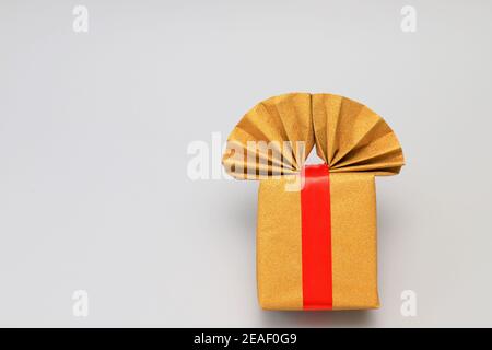 Goldene, gelbe Geschenkbox mit einer leuchtend roten Schleife auf grauem Hintergrund. Geburtstagsgeschenk, Feier, Illuminating und Ultimate Grey 2021 Stockfoto
