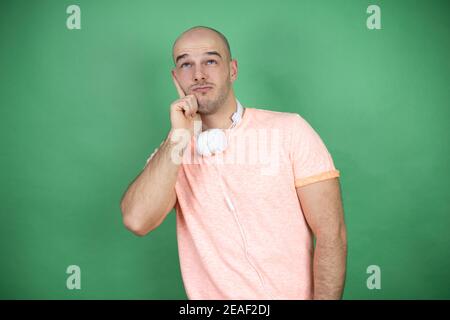 Junge Glatze Mann mit Kopfhörern über grünen Hintergrund denken und Blick zur Seite Stockfoto