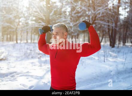 Senioren trainieren im Winter mit Hanteln im Freien. Reifer Bodybuilder arbeitet seine Bizeps im verschneiten Park Stockfoto