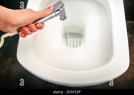 Eine Frau wäscht Toilettenschüssel mit einer hygienischen Dusche, Nahaufnahme. Probleme mit der Desinfektion durch Quarantäne und Isolation von Coronavirus. Brauner Stein Stockfoto