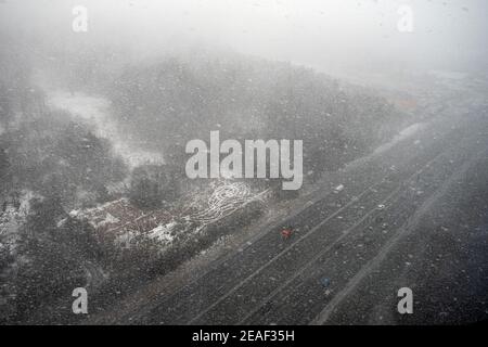 Schneesturm im Wald über eine Straße mit Auto. Blizzard im Winterpark, Draufsicht Stockfoto