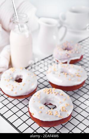 Donuts auf dem Backblech glasiert weiße Schokoladencreme oder Glasur und Flasche mit Milch auf dem Hintergrund Stockfoto