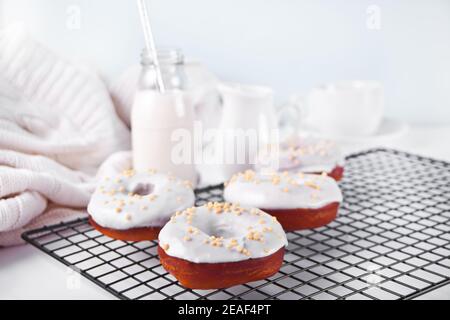 Donuts auf dem Backblech glasiert weiße Schokoladencreme oder Glasur und Flasche mit Milch auf dem Hintergrund Stockfoto