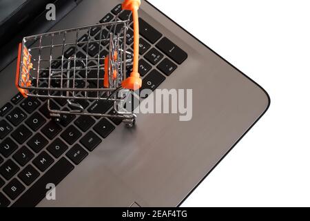 Mini-Einkaufswagen oder Trolley neben dem Laptop. Online-Shopping-Konzept, das Menschen ermöglicht, einfach und schnell zu kaufen. Isoliert auf weißem Hintergrund Stockfoto