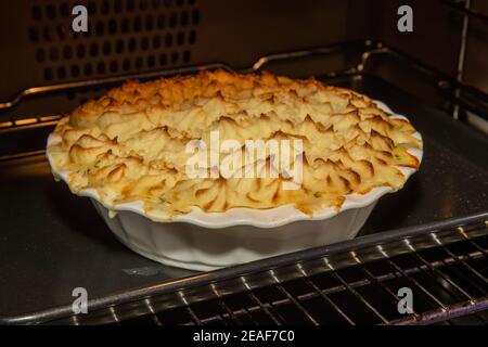 Ein köstlicher Fisch- und Seafood-Kuchen, gekrönt mit goldbrauner Maischkartoffel im Ofen, der gebacken wird, bis er goldbraun ist Stockfoto