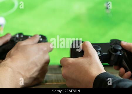 Nahaufnahme Ansicht von Mann und Frau Hände, spielen und halten Video-Konsole Spiel Pad mit Fußballspiel, grüner Bildschirm-Fernseher auf background.Friends Hobbi Stockfoto