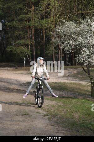 Happy girl auf Beinen verbreiten Spaß reitet ein Fahrrad in der Nähe eines blühenden Baumes. Gesunde aktive Lebensweise. Frische Luft Radfahren im Wald Stockfoto