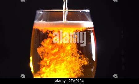 Gießen Sie helles Bier in ein Glas auf dunklem Grund. Innenglow Stockfoto