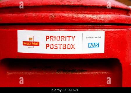 Traditionelle rote britische Royal Mail Postbox mit Aufkleber. Vorrangiges Postfach. Unterstützung des NHS während der Covid-Pandemie von 2020 2021 Stockfoto