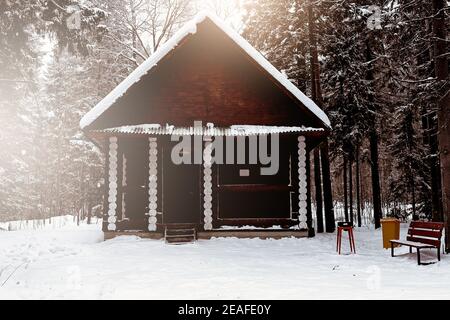 Holzhaus zwischen Bäumen im Winterwald. Blockhütte. Gehäuse aus natürlichen Baustoffen. Umweltfreundliche Konstruktion. Stockfoto