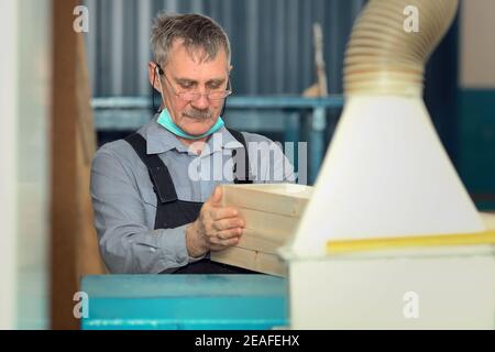 Ein älterer Zimmermann mit kaukasischem Aussehen arbeitet in einer Schreinerei. Die Bearbeitung der Bretter auf der Drehbank. Stockfoto