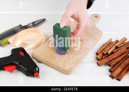 Floristin bei der Arbeit: Frau zeigt, wie man moderne, minimalistische Blumendekoration mit Lilienblume, rosa Canina Zweige und Zimt-Sticks zu machen. Schritt für Schritt Stockfoto