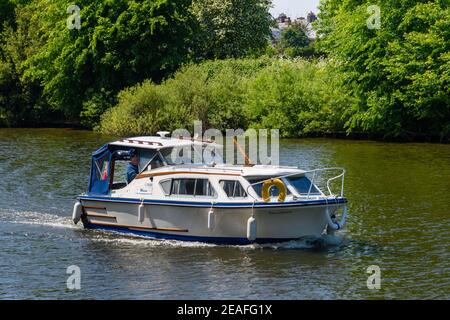 Boot (Freizeit Cruiser) Segeln auf landschaftlich schönen Fluss Ouse an sonnigen Sommertag, 2 Männer im Cockpit auf entspannende Reise - York, North Yorkshire, England, Großbritannien. Stockfoto