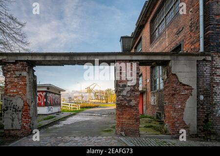 Ein gemauertes Tor in einem alten Industriegebiet mit Schiffsladekran im Hintergrund. Goldene Stunde im Ostseehafen Danzig, Polen. Stockfoto