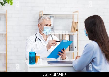 Arzt in weißen medizinischen Uniform und Schutzmaske diskutieren Ergebnisse Oder Symptome bei Frauen Stockfoto